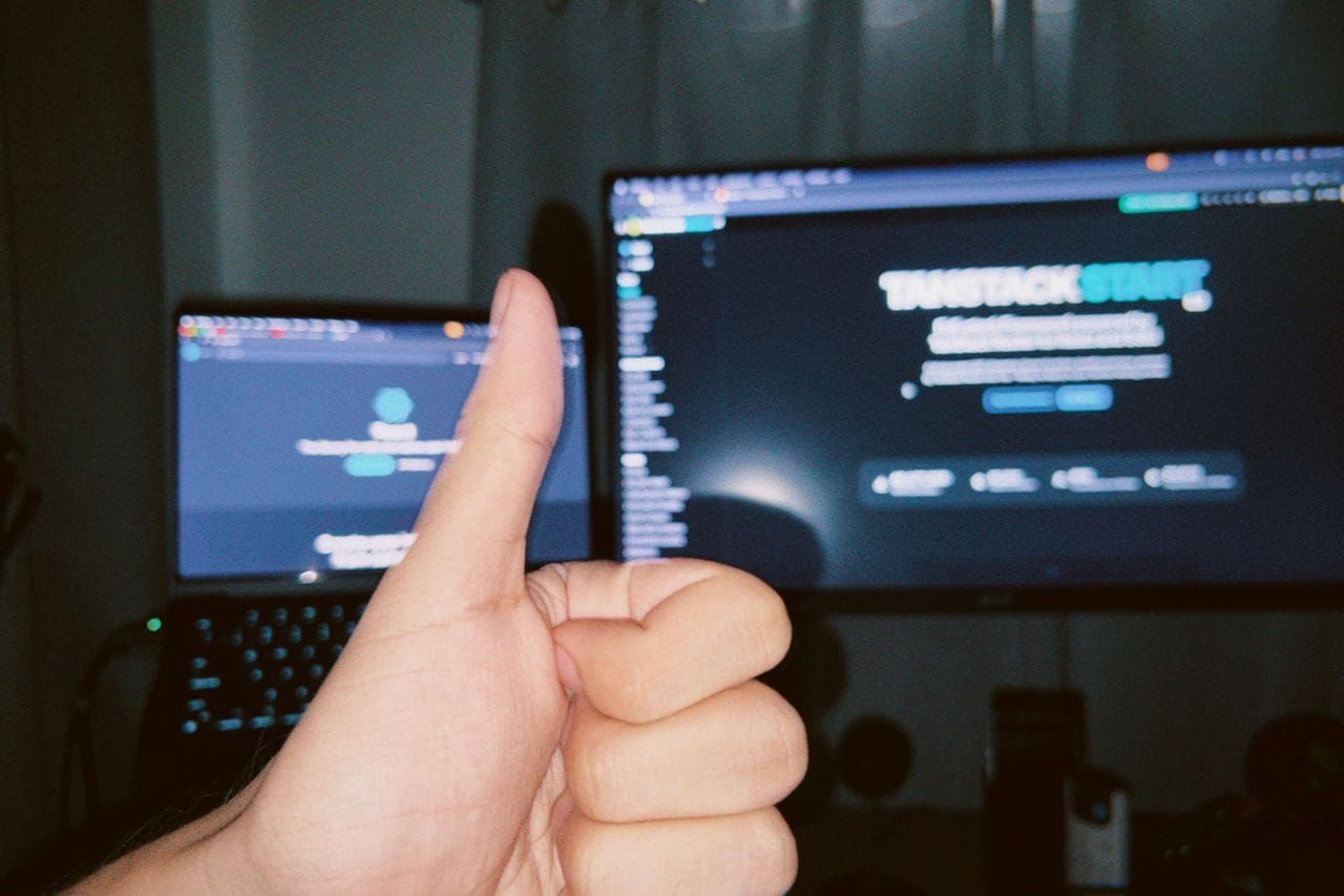 A person giving a thumbs up with a laptop and monitor displaying the TanStack Start homepage in the background
